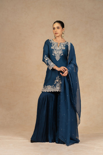 Peacock blue embroidered sharara suit with silk kurta, pleated sharara, and organza dupatta featuring intricate dabka, kasab, sequins, and pearl embellishments – perfect for festive and wedding occasions.