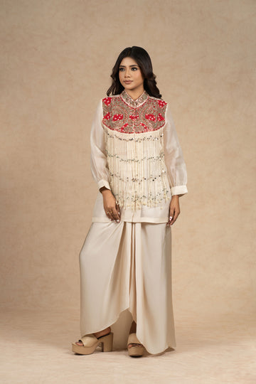 Model wearing an ivory organza Indowestern ensemble featuring a bustier and draped skirt, adorned with intricate dori work, pearl embellishments, and vibrant red embroidered detailing on the yoke.