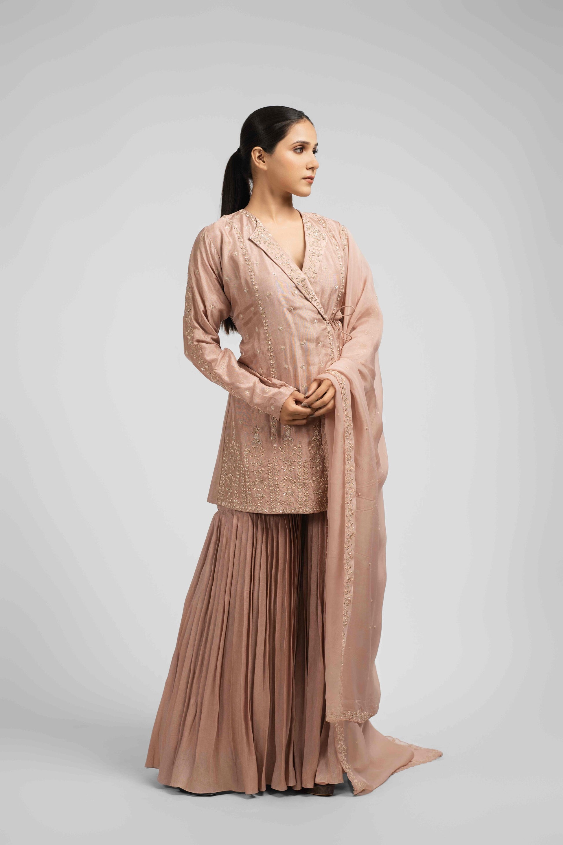 Ash rose pink sharara suit featuring an angrakha-style kurta with lapel collar, intricate zardozi, kasab, pearl, and sequin work, paired with pleated sharara pants and an organza dupatta for a timeless festive look.