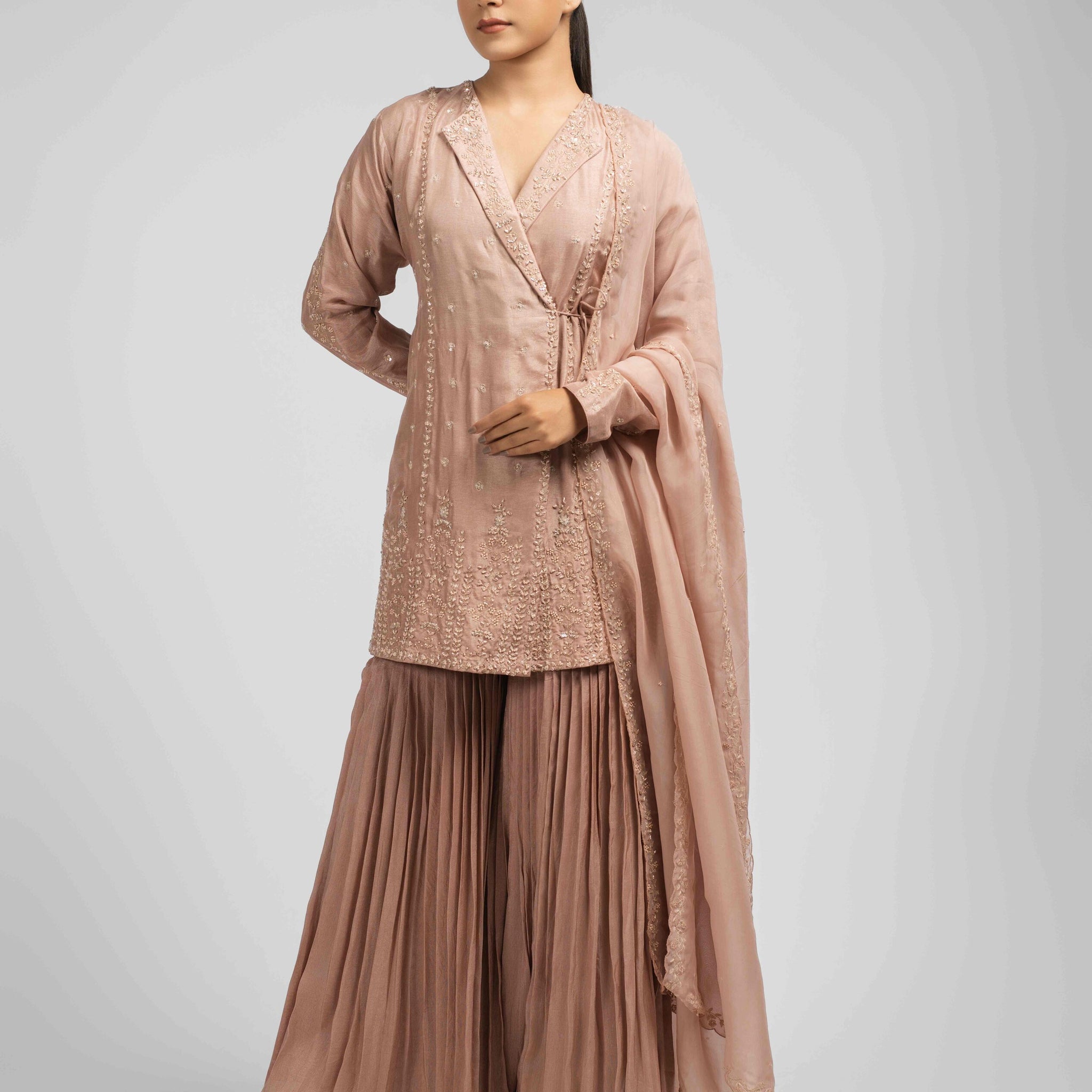 Ash rose pink sharara suit featuring an angrakha-style kurta with lapel collar, intricate zardozi, kasab, pearl, and sequin work, paired with pleated sharara pants and an organza dupatta for a timeless festive look.