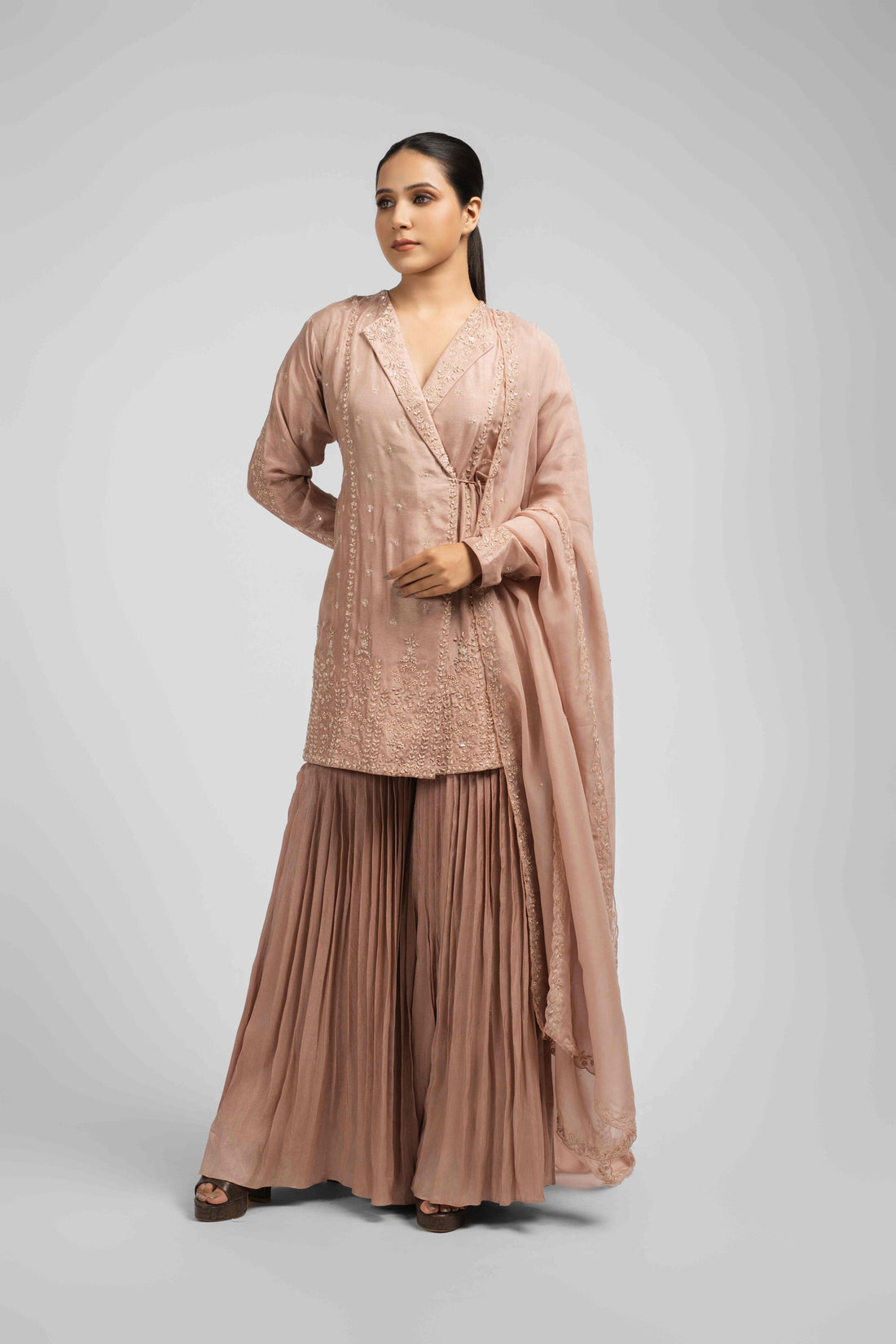 Ash rose pink sharara suit featuring an angrakha-style kurta with lapel collar, intricate zardozi, kasab, pearl, and sequin work, paired with pleated sharara pants and an organza dupatta for a timeless festive look.