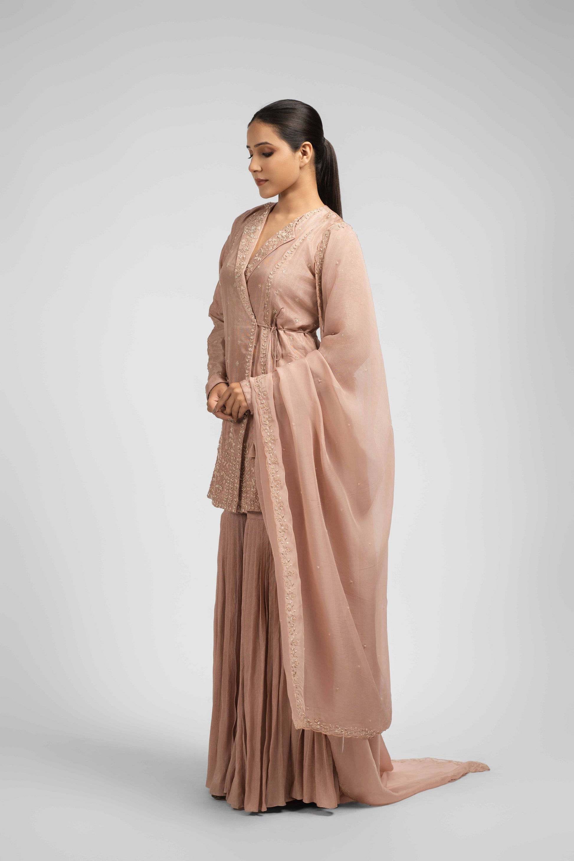 Ash rose pink sharara suit featuring an angrakha-style kurta with lapel collar, intricate zardozi, kasab, pearl, and sequin work, paired with pleated sharara pants and an organza dupatta for a timeless festive look.
