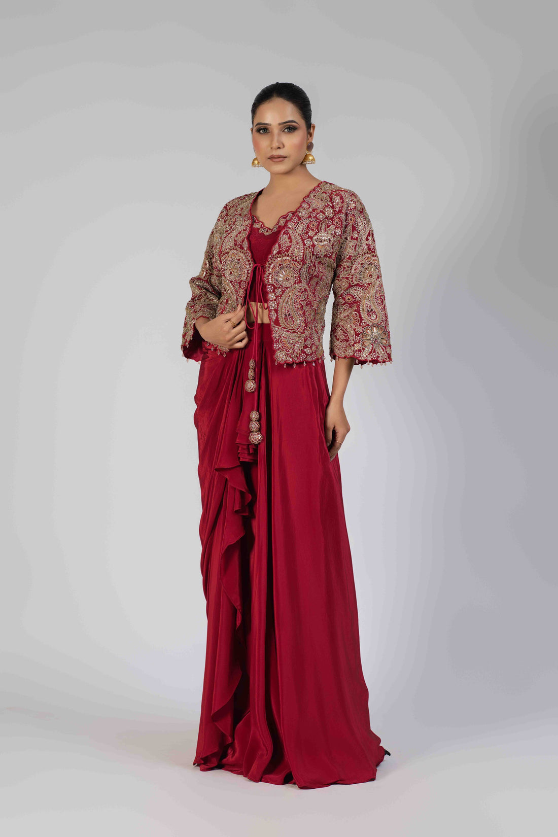 Blood red Indowestern jacket set with a sleeveless crop blouse, short embellished jacket, and draped skirt featuring intricate kasab, zardozi, sequins, pearl, and thread work. Perfect for festive and wedding occasions.