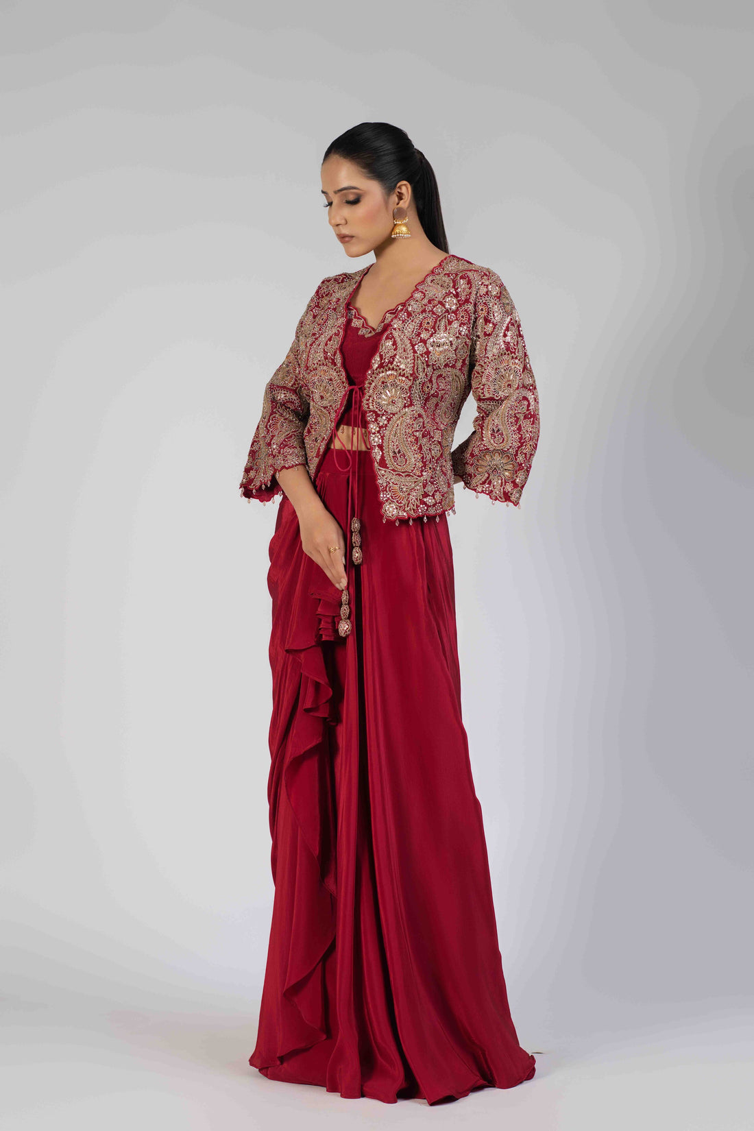 Blood red Indowestern jacket set with a sleeveless crop blouse, short embellished jacket, and draped skirt featuring intricate kasab, zardozi, sequins, pearl, and thread work. Perfect for festive and wedding occasions.