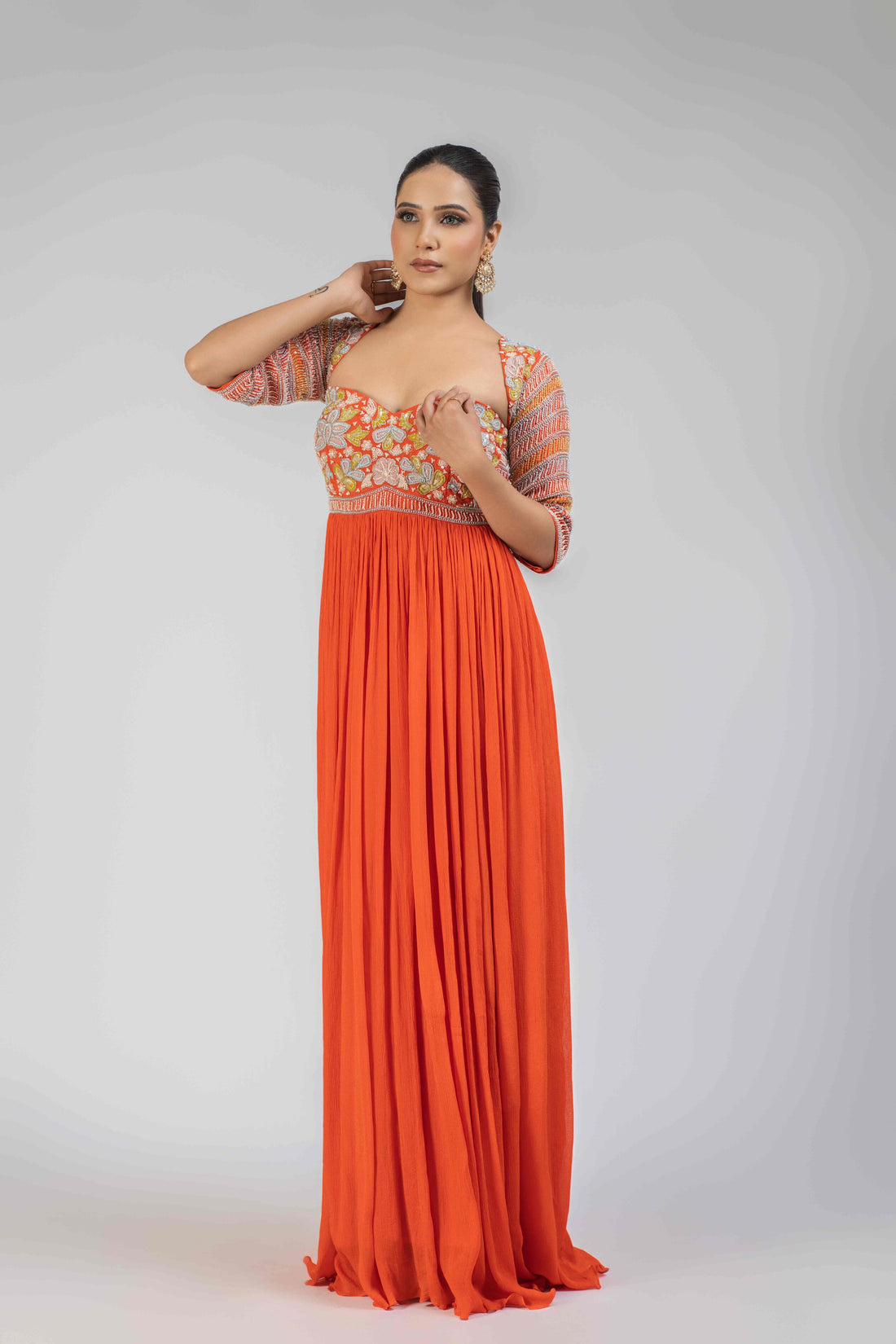 Orange chinnon anarkali gown with an embellished bodice, elbow-length sleeves, and an organza dupatta adorned with pearls, kasab, sequins, and colorful patchwork, ideal for festive and wedding occasions.