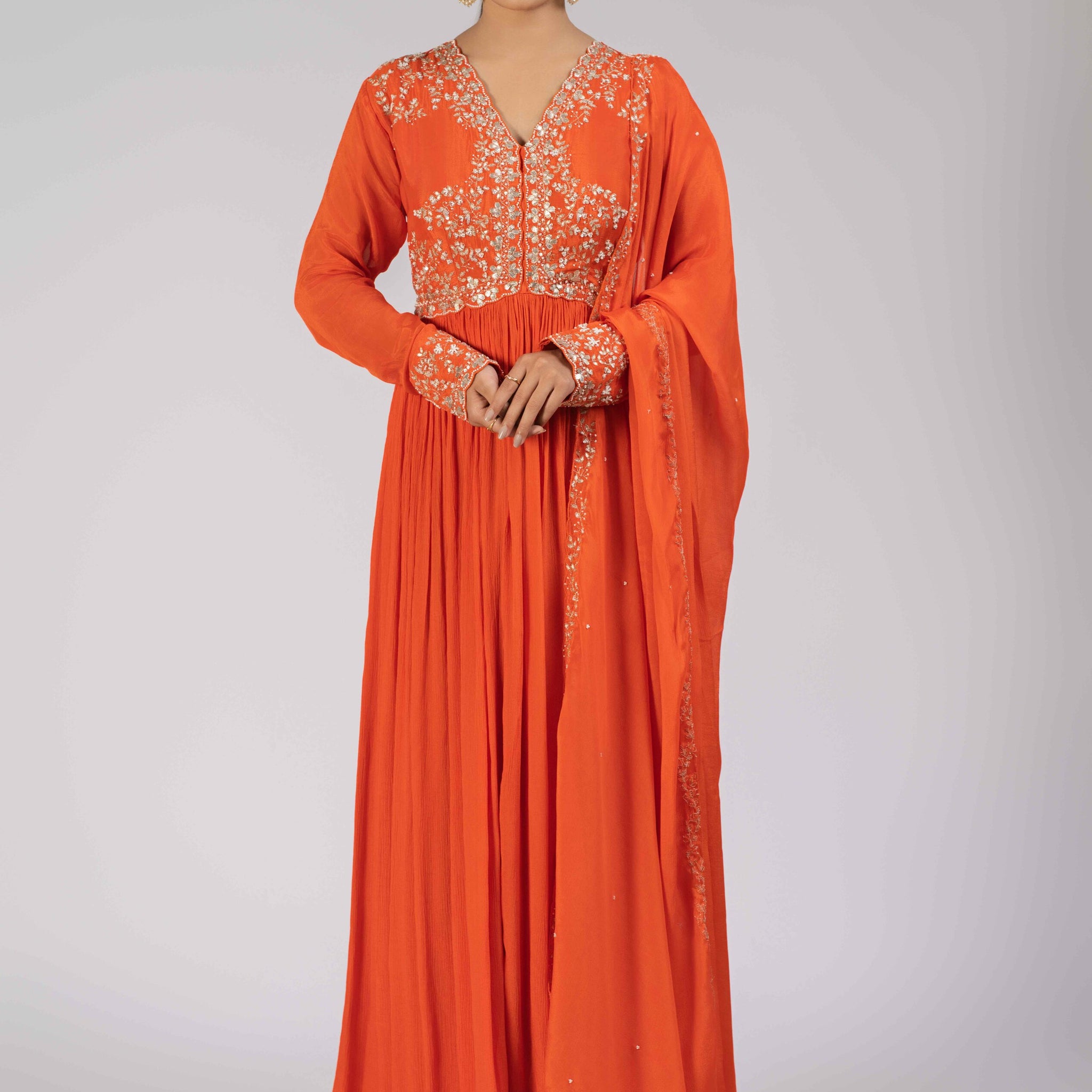 A model wearing an orange chinnon gota work gathered suit with an embellished bodice, sleeve cuffs, and a matching chinnon dupatta adorned with kasab, gotta patti, pearls, and sequins, perfect for festive and wedding occasions.