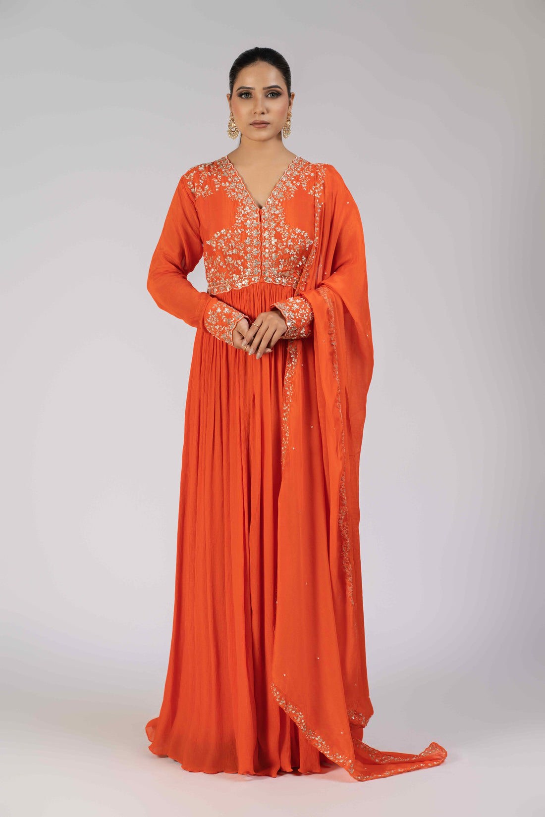 A model wearing an orange chinnon gota work gathered suit with an embellished bodice, sleeve cuffs, and a matching chinnon dupatta adorned with kasab, gotta patti, pearls, and sequins, perfect for festive and wedding occasions.