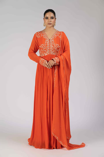 A model wearing an orange chinnon gota work gathered suit with an embellished bodice, sleeve cuffs, and a matching chinnon dupatta adorned with kasab, gotta patti, pearls, and sequins, perfect for festive and wedding occasions.