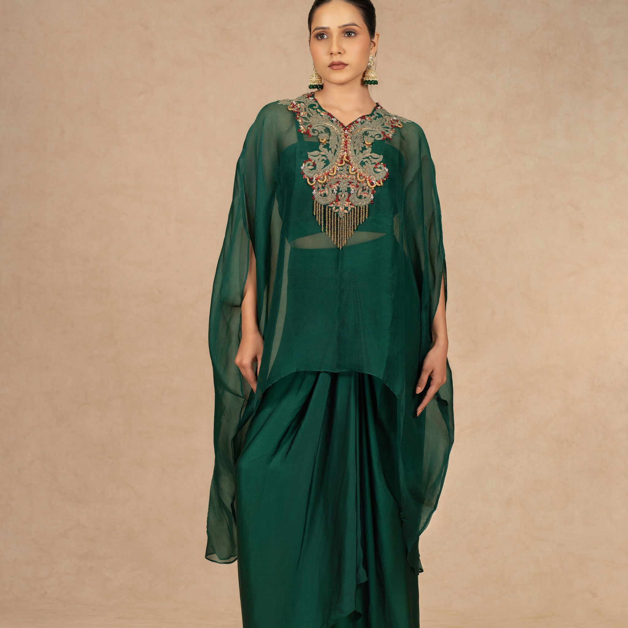 Model wearing a Bottle Green Organza Indowestern outfit with an embroidered bustier and drape skirt, featuring sheer cape sleeves.