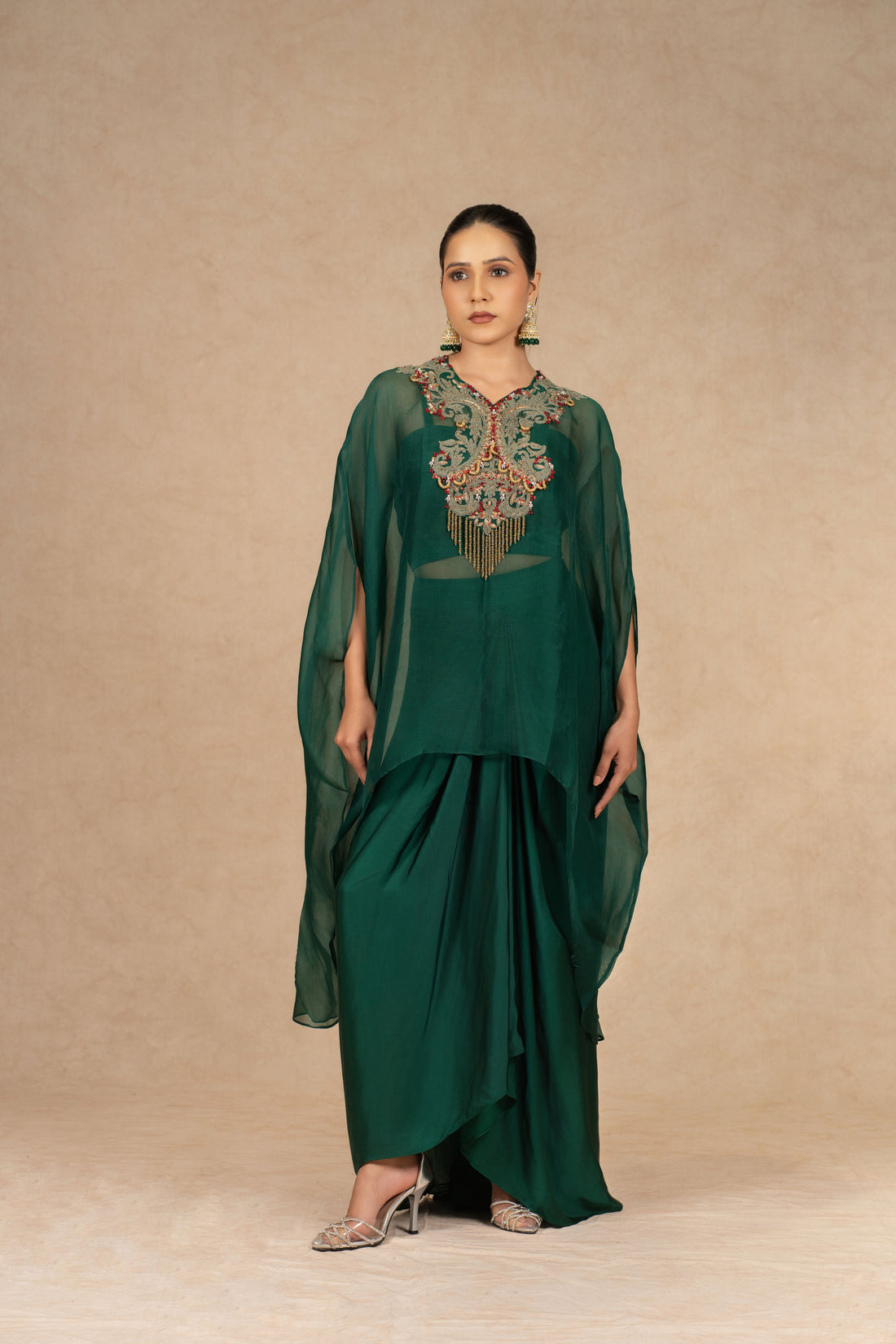 Model wearing a Bottle Green Organza Indowestern outfit with an embroidered bustier and drape skirt, featuring sheer cape sleeves.