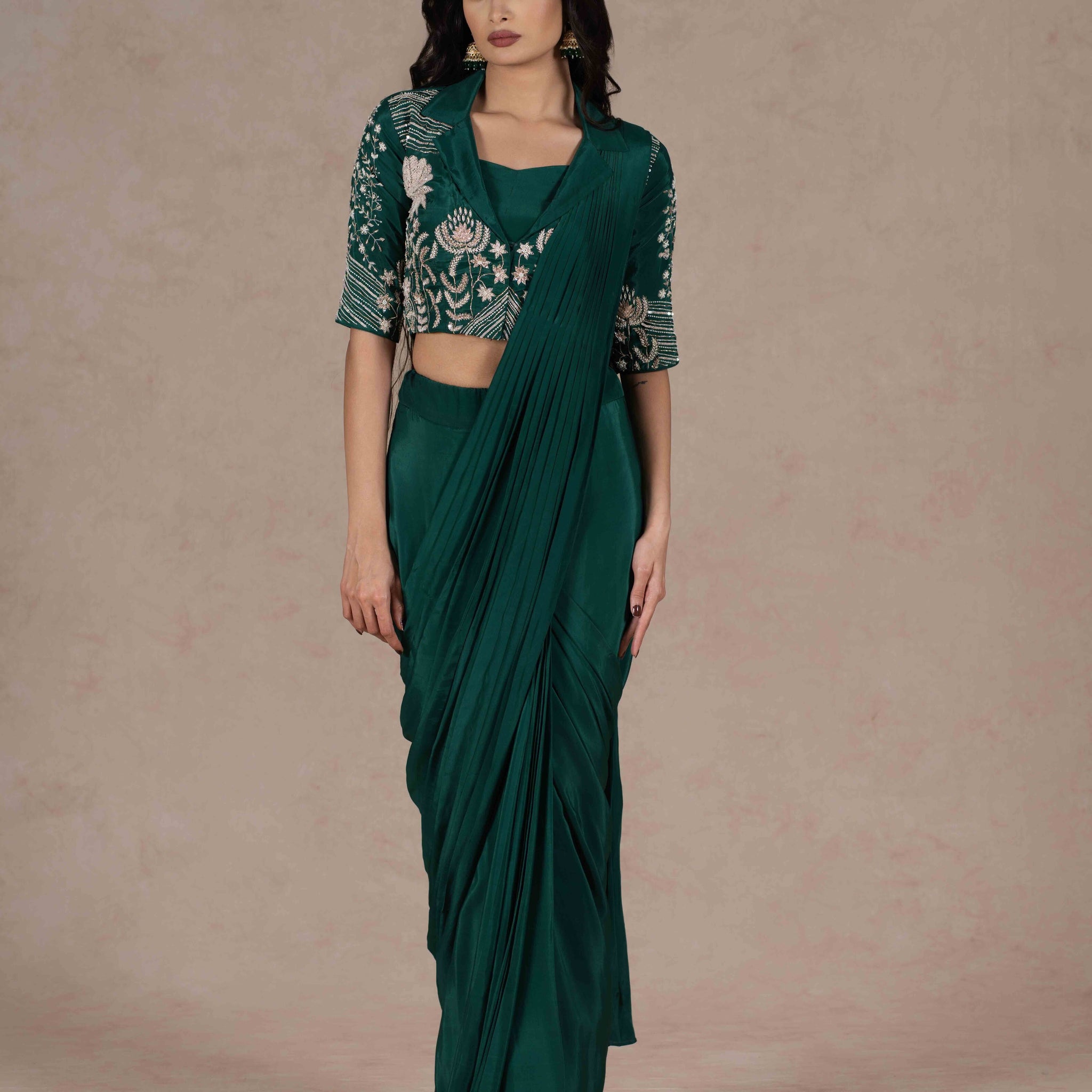 Bottle green pre-draped saree with a zardozi-embroidered cropped lapel collar jacket and plain strappy bustier, blending modern cuts with Indian tradition for a chic look.