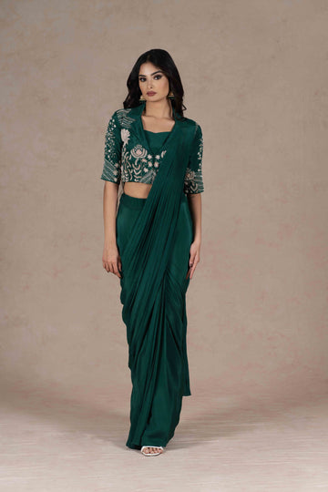 Bottle green pre-draped saree with a zardozi-embroidered cropped lapel collar jacket and plain strappy bustier, blending modern cuts with Indian tradition for a chic look.