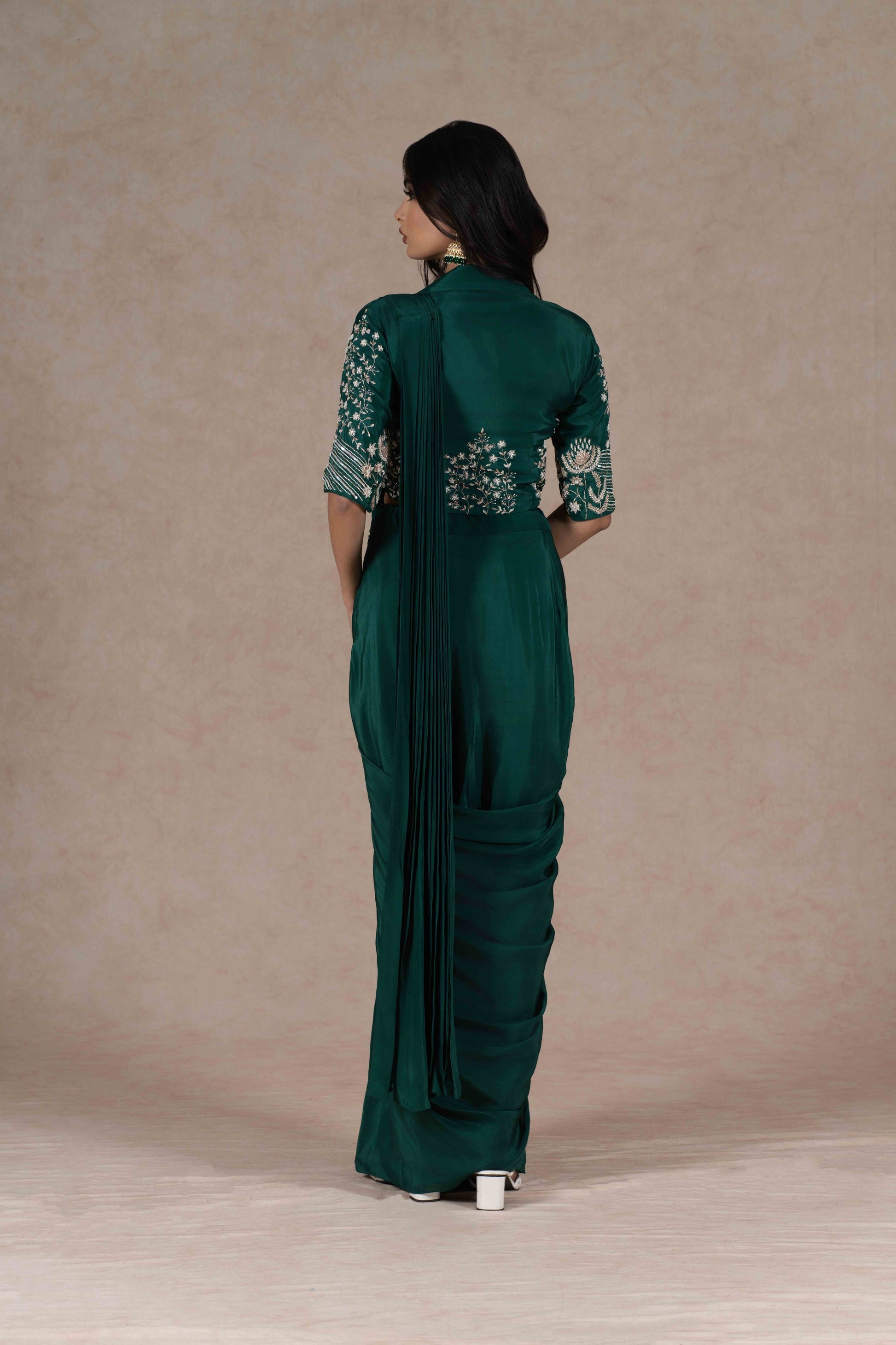 Bottle green pre-draped saree with a zardozi-embroidered cropped lapel collar jacket and plain strappy bustier, blending modern cuts with Indian tradition for a chic look.