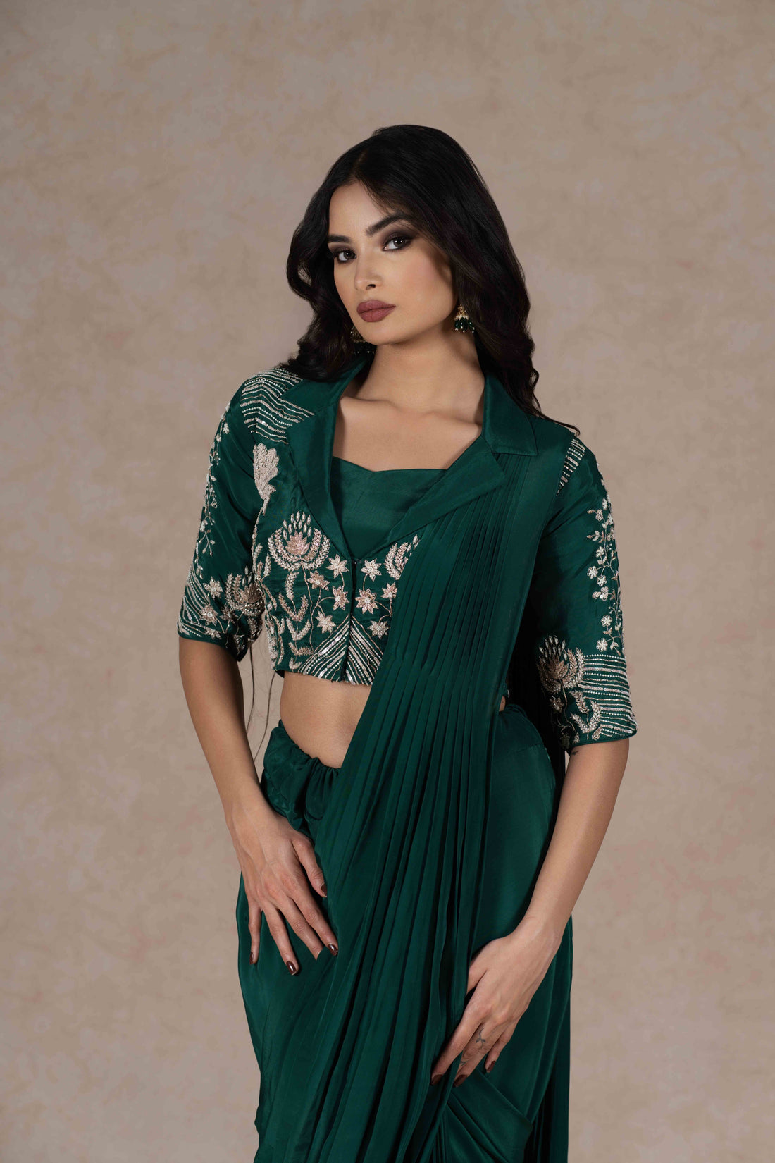 Bottle green pre-draped saree with a zardozi-embroidered cropped lapel collar jacket and plain strappy bustier, blending modern cuts with Indian tradition for a chic look.