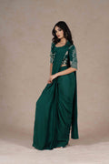 Bottle green pre-draped saree with a zardozi-embroidered cropped lapel collar jacket and plain strappy bustier, blending modern cuts with Indian tradition for a chic look.