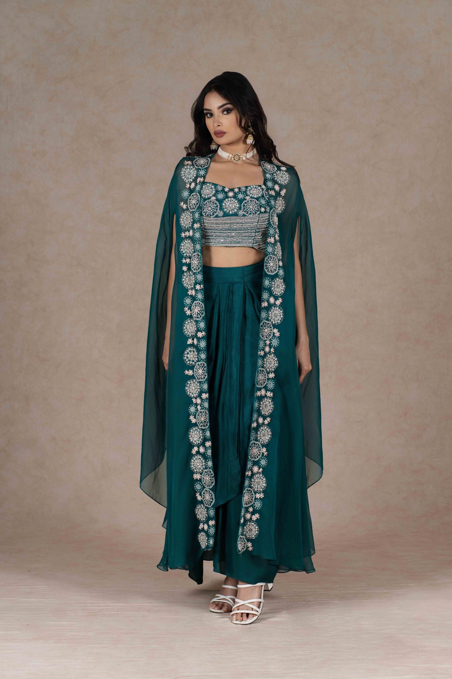 A full view of the emerald green three-piece set, featuring an embroidered bustier, sheer cape, and draped skirt.