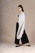  The semi-sheer off-white tissue cape drapes elegantly over the shoulders, revealing the sleeveless black bustier underneath, while the wide-hemmed black palazzo pants ensure both style and comfort.