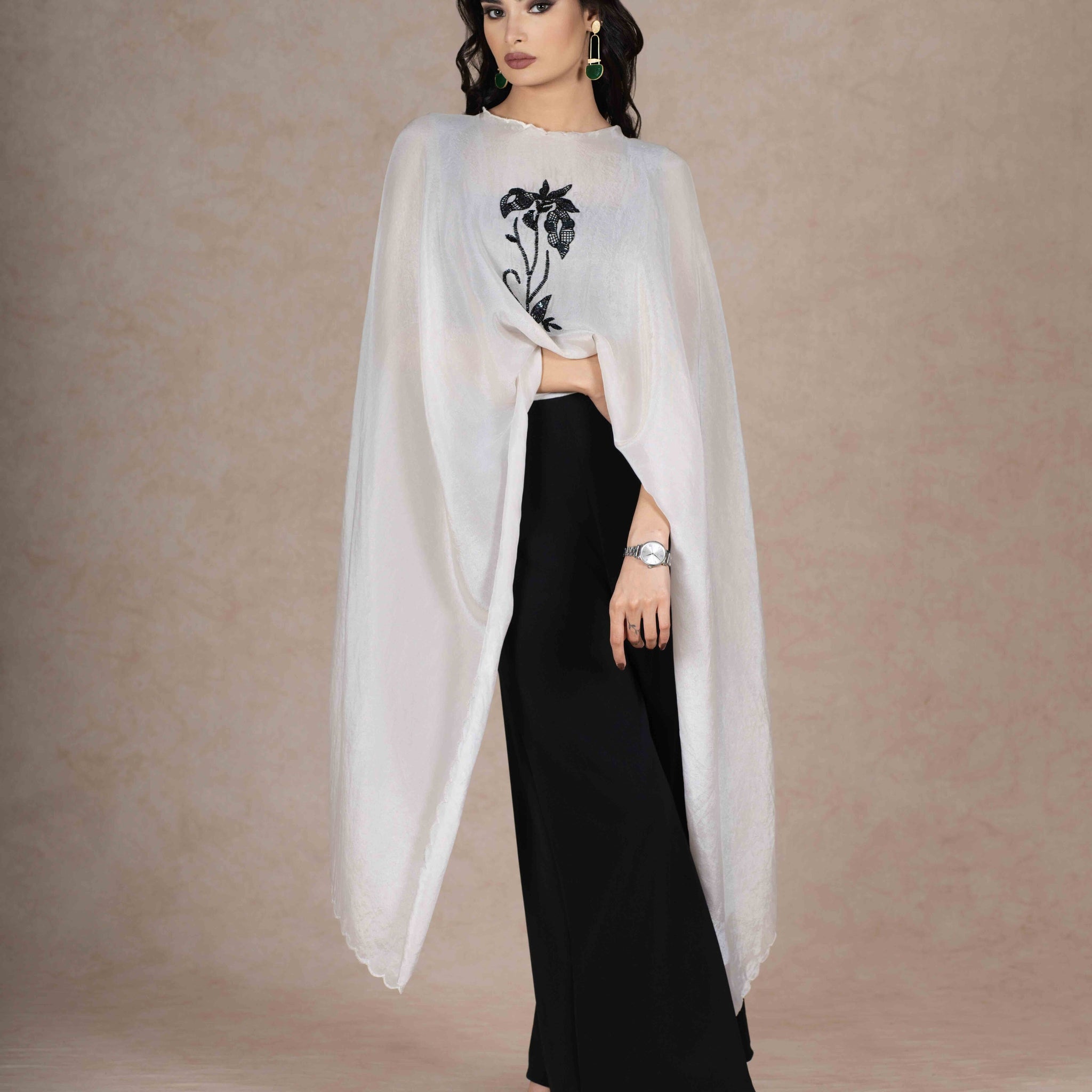 A sophisticated ensemble featuring a soft white tissue cape intricately hand-embroidered with black sequins, attached to black flared palazzo pants for a seamless, modern silhouette.