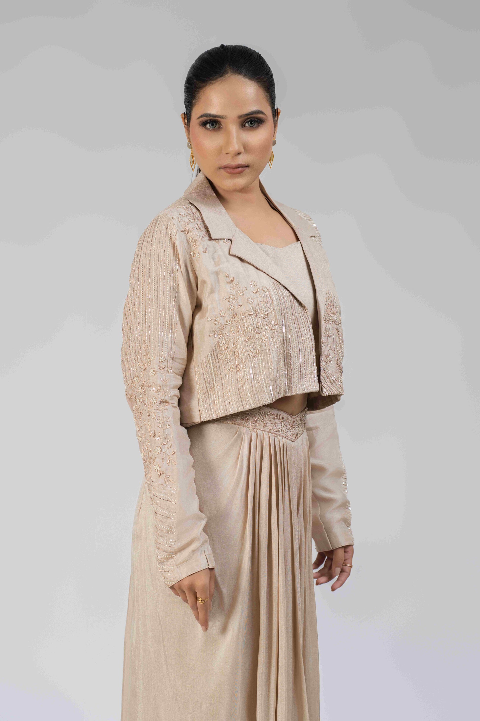  Ivory silk Indo-western set featuring an embellished blazer with pearl, kasab, sequin, and pitai work, paired with a sleeveless crop top and a pleated dhoti-style drape skirt.