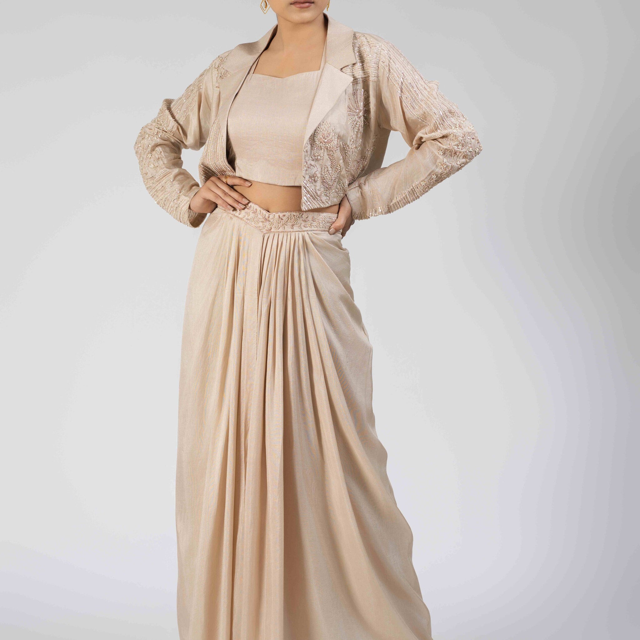  Ivory silk Indo-western set featuring an embellished blazer with pearl, kasab, sequin, and pitai work, paired with a sleeveless crop top and a pleated dhoti-style drape skirt.