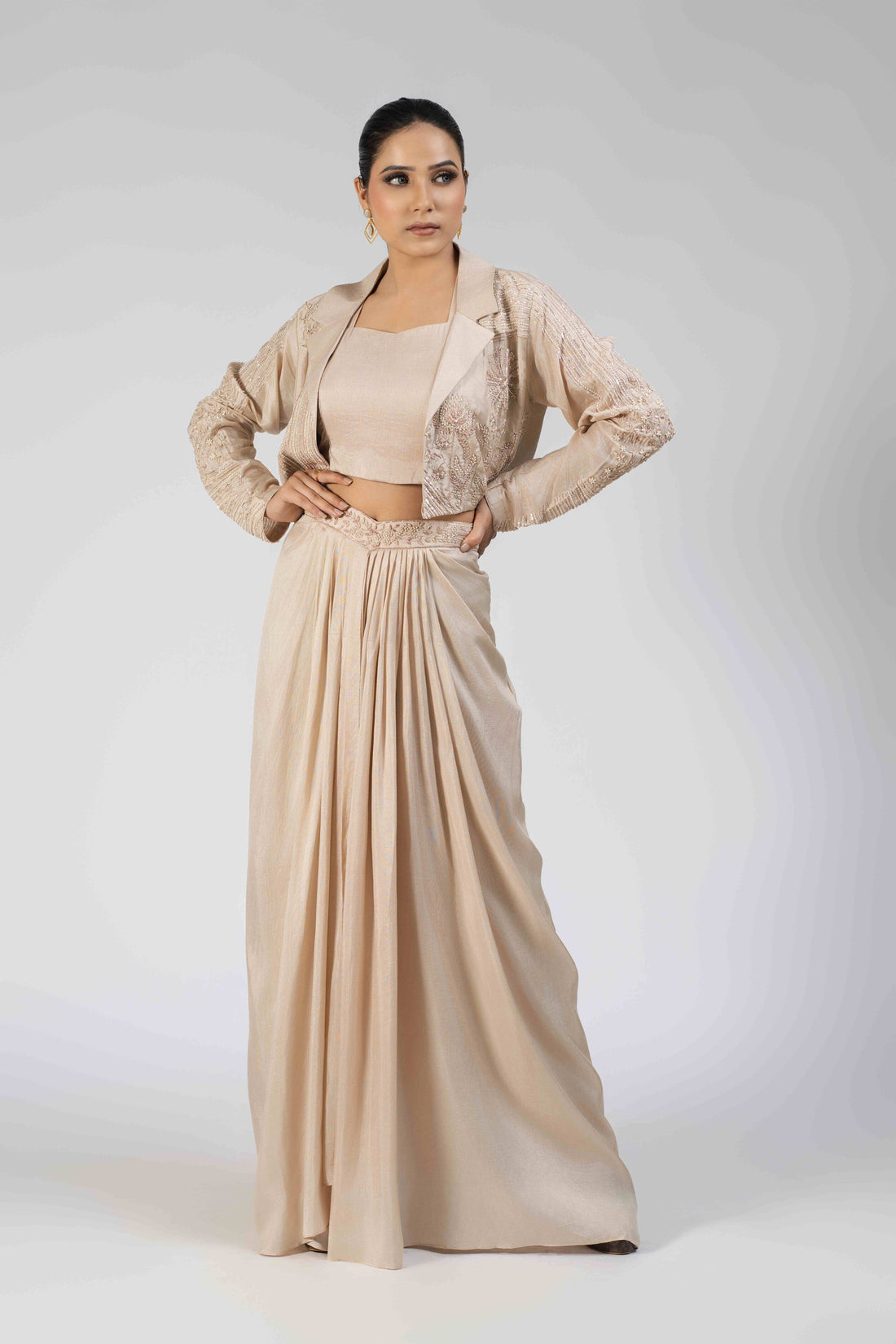  Ivory silk Indo-western set featuring an embellished blazer with pearl, kasab, sequin, and pitai work, paired with a sleeveless crop top and a pleated dhoti-style drape skirt.