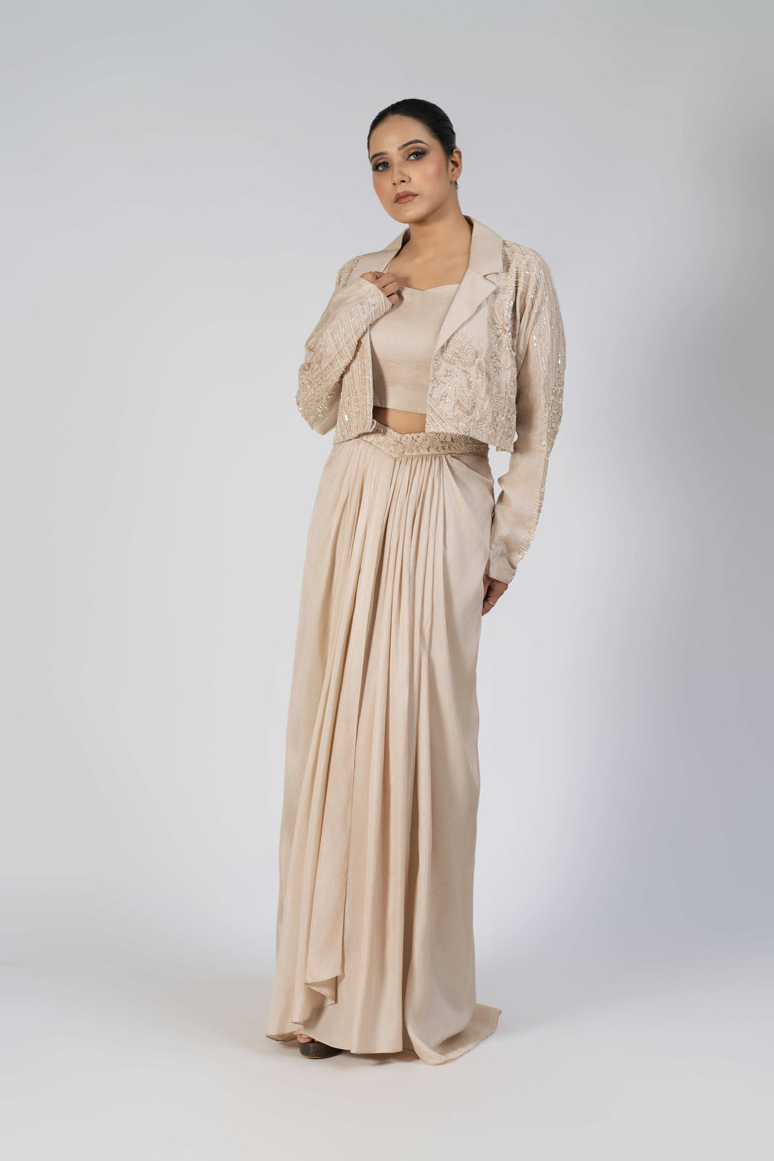  Ivory silk Indo-western set featuring an embellished blazer with pearl, kasab, sequin, and pitai work, paired with a sleeveless crop top and a pleated dhoti-style drape skirt.