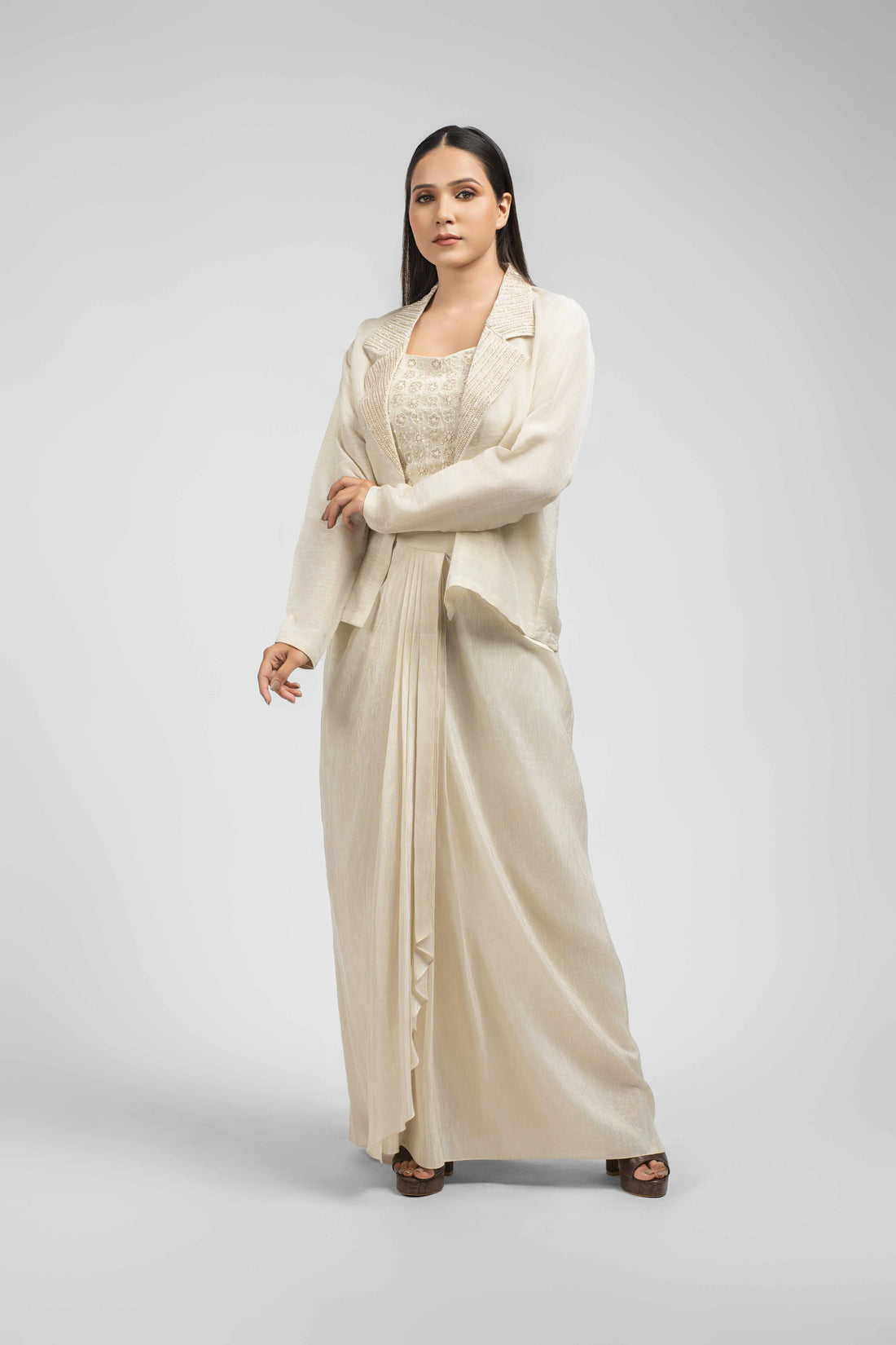Ivory Linen Tissue Blazer Set with Drape Skirt featuring an embellished blazer, a sleeveless crop top, and a pleated dhoti skirt. Embellished with pearls, kasab, and cutdana, perfect for festive or formal occasions.