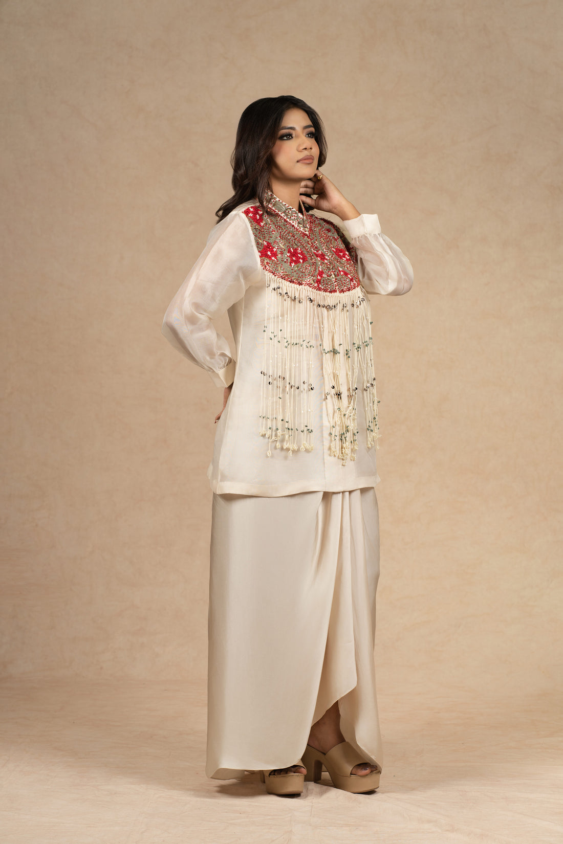  Model wearing an ivory organza Indowestern ensemble featuring a bustier and draped skirt, adorned with intricate dori work, pearl embellishments, and vibrant red embroidered detailing on the yoke.