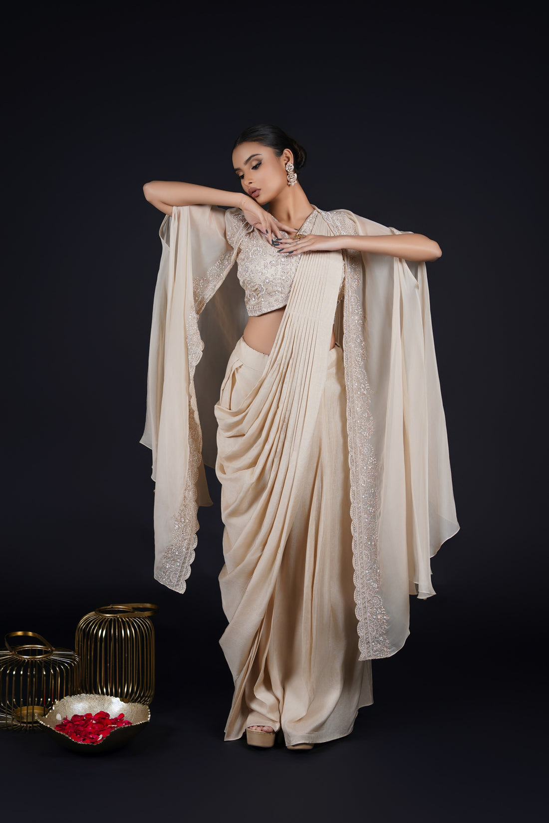 Ivory pre-draped saree paired with an embellished blouse and cape, featuring kasab, sequins, cutdana, pearls, and thread detailing. Perfect for festive and wedding occasions.