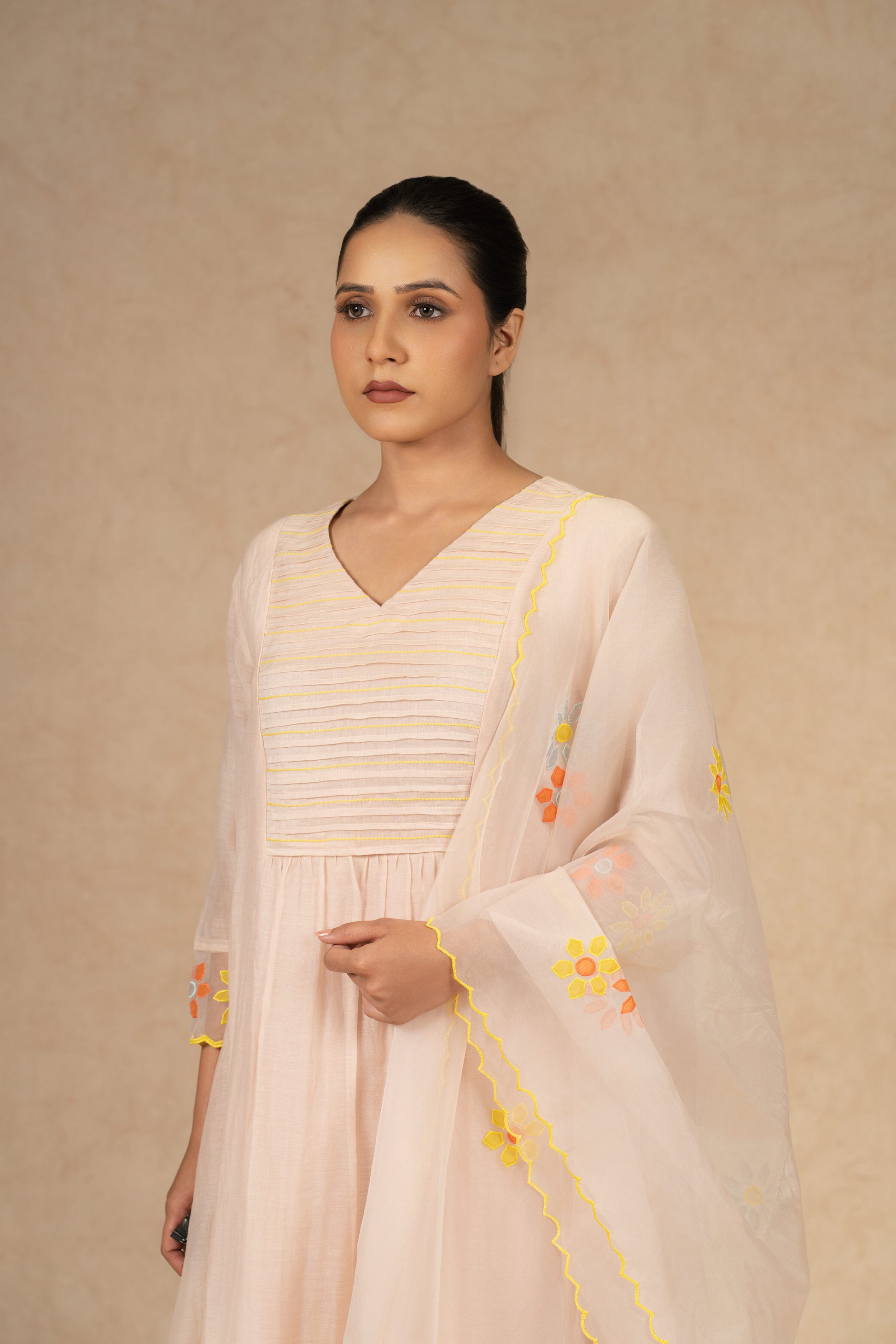 Light peach Chanderi suit with pants and an organza dupatta featuring floral embroidery, pearl embellishments, and pleated detailing, perfect for festive and formal occasions.