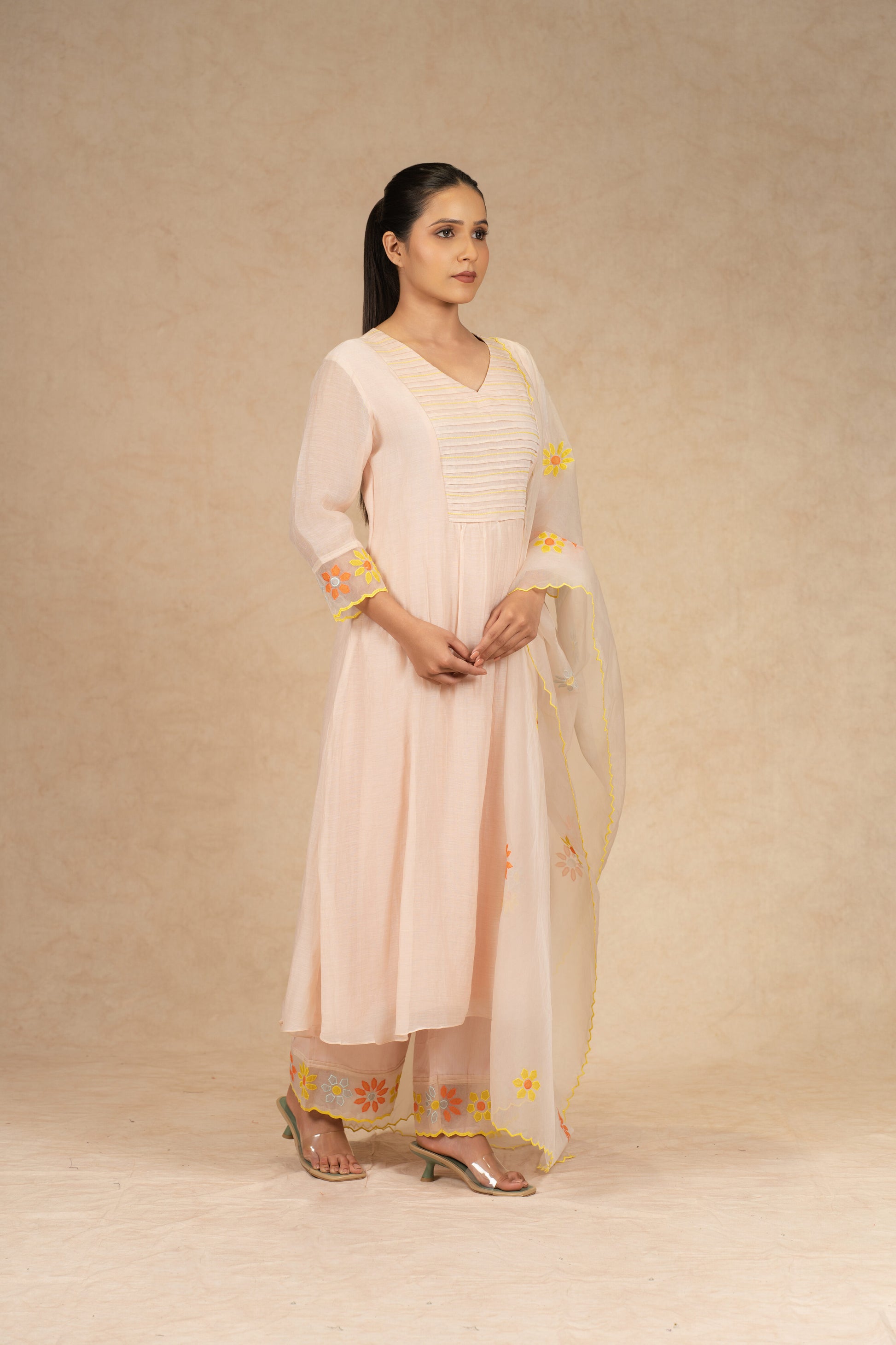 Light peach Chanderi suit with pants and an organza dupatta featuring floral embroidery, pearl embellishments, and pleated detailing, perfect for festive and formal occasions.