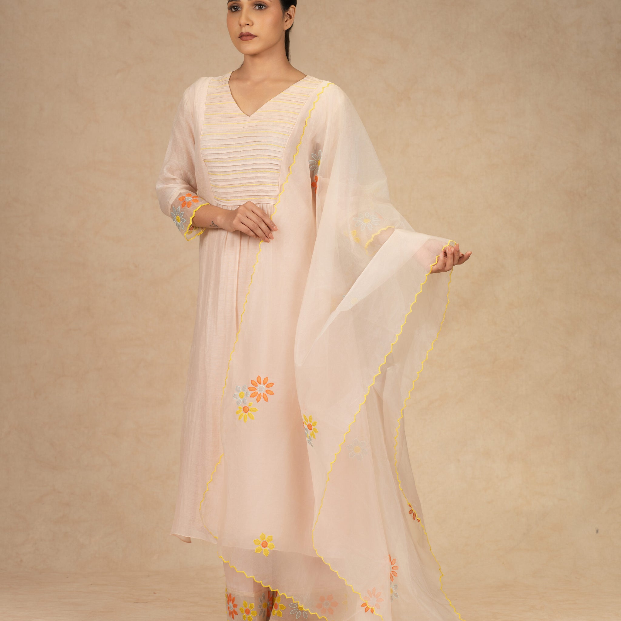 Light peach Chanderi suit with pants and an organza dupatta featuring floral embroidery, pearl embellishments, and pleated detailing, perfect for festive and formal occasions.