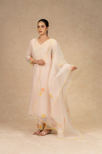 Light peach Chanderi suit with pants and an organza dupatta featuring floral embroidery, pearl embellishments, and pleated detailing, perfect for festive and formal occasions.