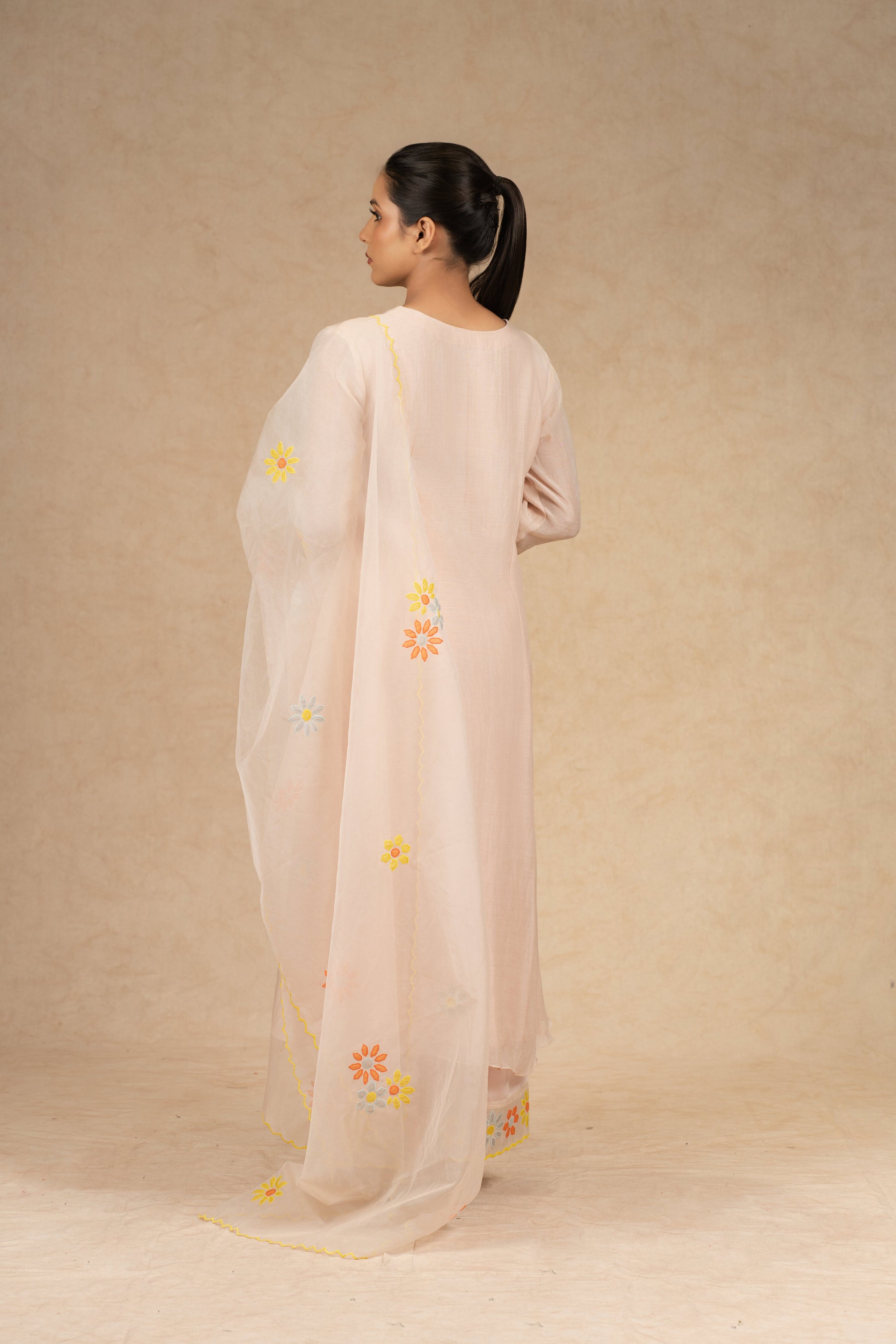 Light peach Chanderi suit with pants and an organza dupatta featuring floral embroidery, pearl embellishments, and pleated detailing, perfect for festive and formal occasions.