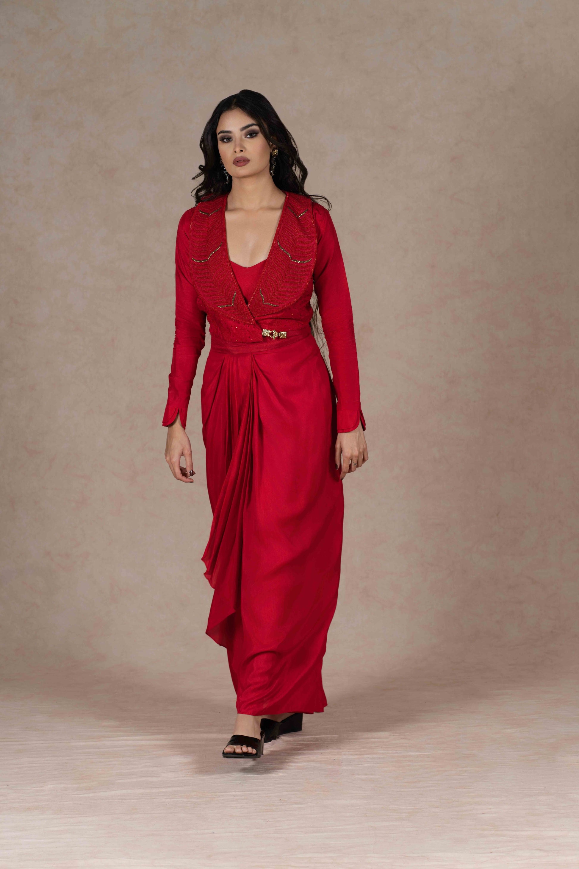 Model wearing the red Indo-western three-piece set, featuring a structured embroidered jacket, buckle fastening, and fluid draped skirt for an elegant evening look.