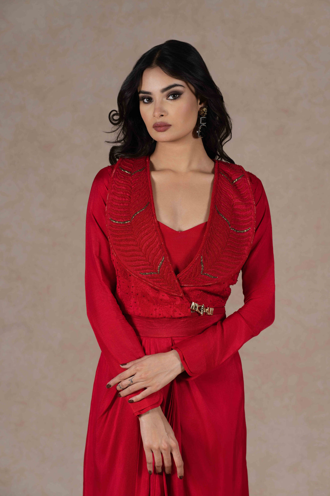 Red Indo-western three-piece set with an embroidered lapel collar jacket, sequined bustier, and draped skirt, blending tradition with modern elegance.