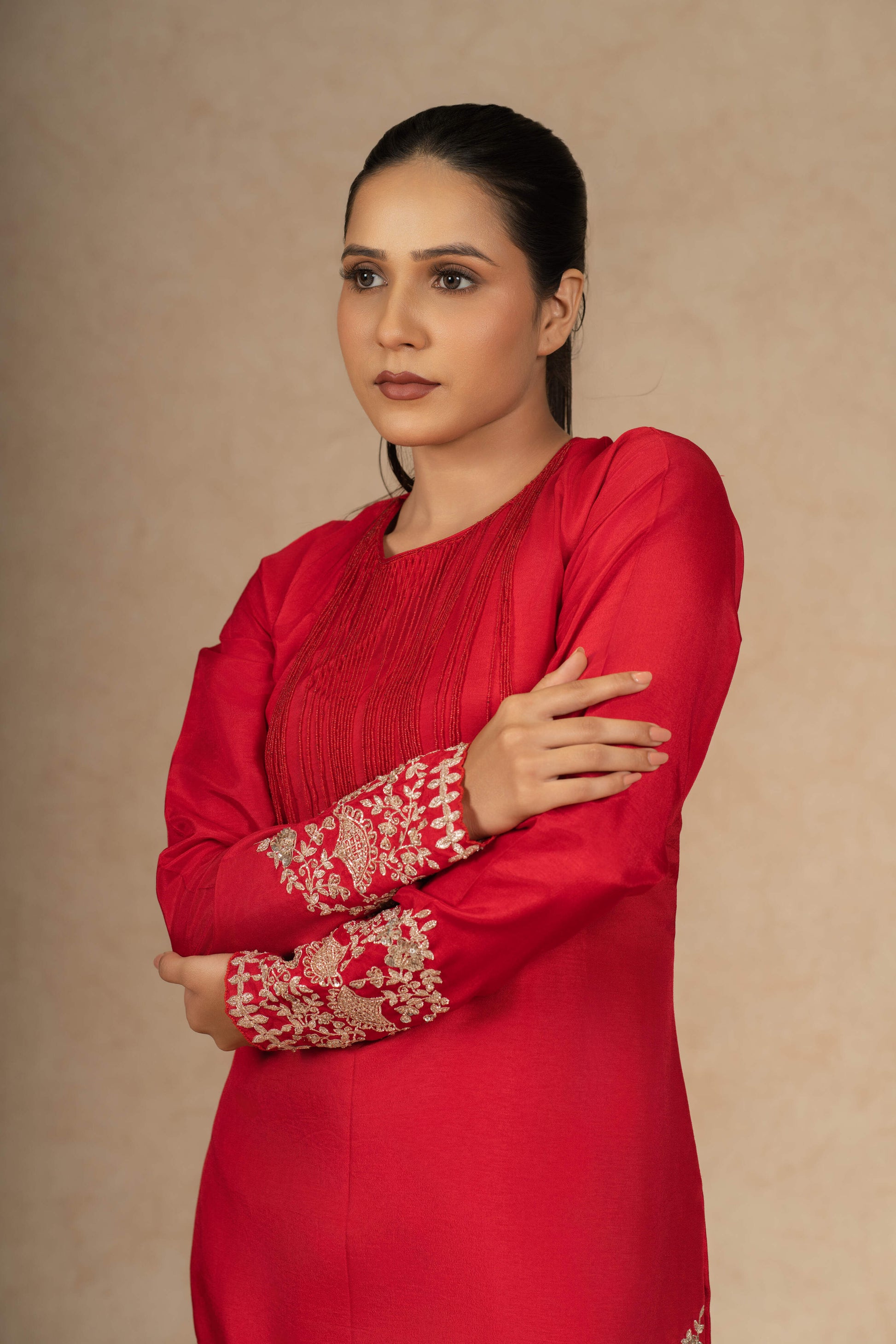 Close-up of a model in a red silk suit, emphasizing the fine embroidery on the sleeves and the luxurious texture of the fabric.