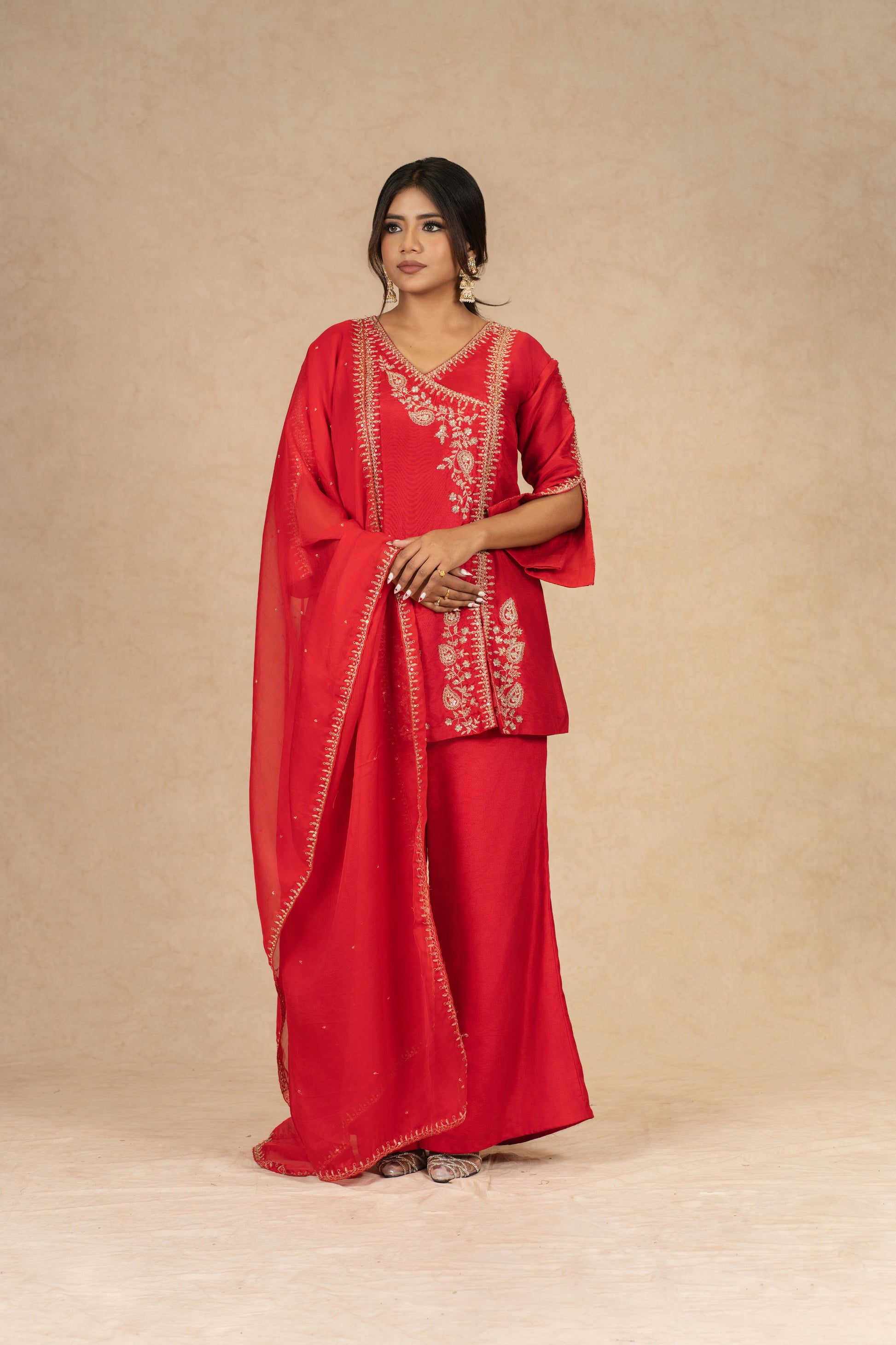 Elegant pose in Red Silk Suit featuring flared pants and an organza dupatta with dabka, sequins, and pearl embellishments.
