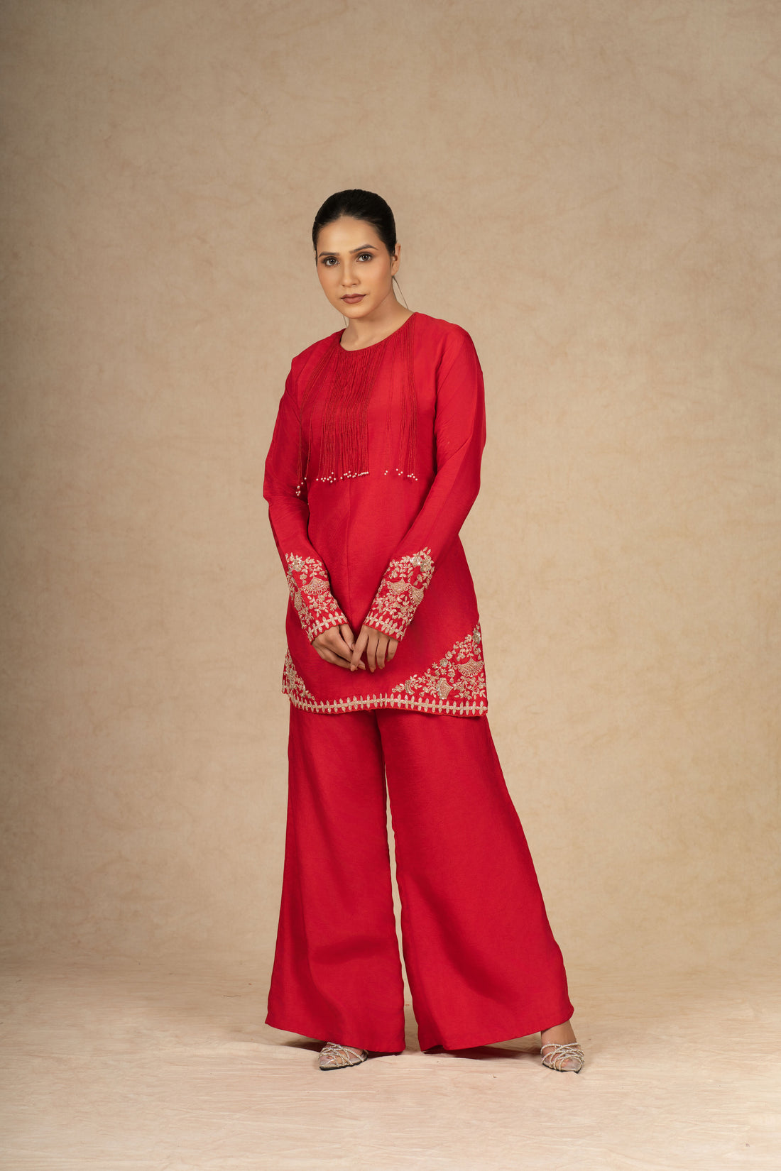 Model posing in a vibrant red silk suit with intricate embroidery on the sleeves and hem, paired with wide-leg pants for a stylish look.