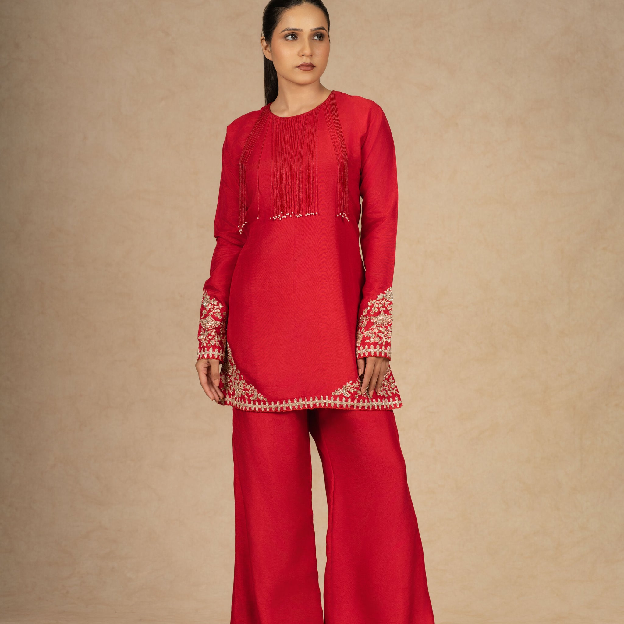 Model posing in a vibrant red silk suit with intricate embroidery on the sleeves and hem, paired with wide-leg pants for a stylish look.