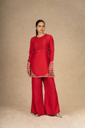 Model posing in a vibrant red silk suit with intricate embroidery on the sleeves and hem, paired with wide-leg pants for a stylish look.