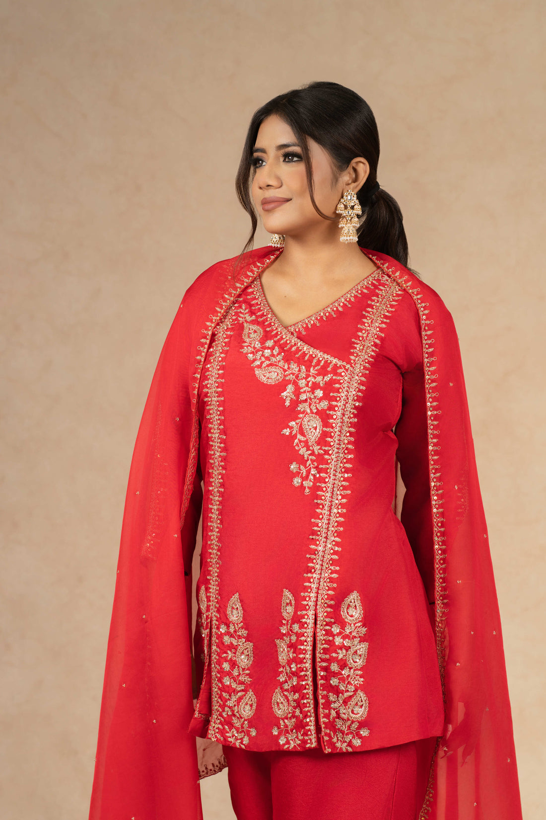 Elegant pose in Red Silk Suit featuring flared pants and an organza dupatta with dabka, sequins, and pearl embellishments.
