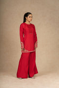 Side view of a model wearing a red silk suit, highlighting the rich fabric and detailed embroidery on the sleeves and hem.