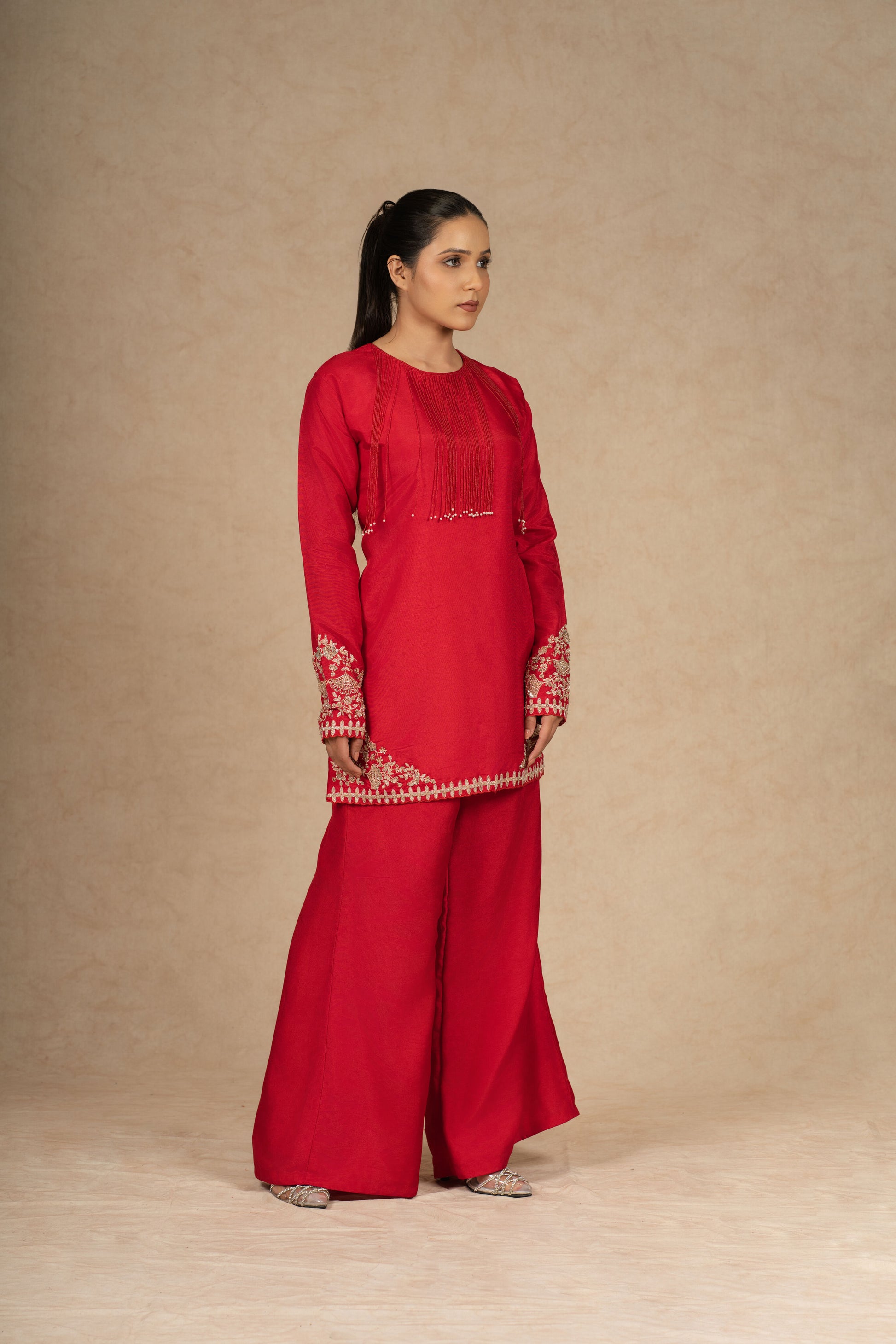 Side view of a model wearing a red silk suit, highlighting the rich fabric and detailed embroidery on the sleeves and hem.