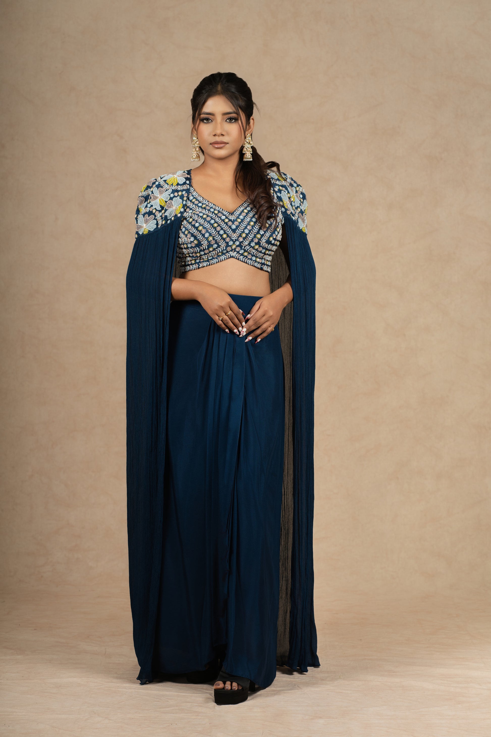 Model gracefully posing in a Royal Blue Indo-Western outfit featuring a heavily embellished blouse, pleated skirt, and a dramatic cape-style drape.