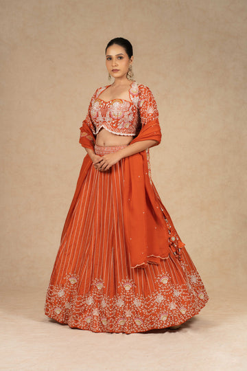 Designer rust lehenga choli with intricate embroidery, paired with a matching organza dupatta.