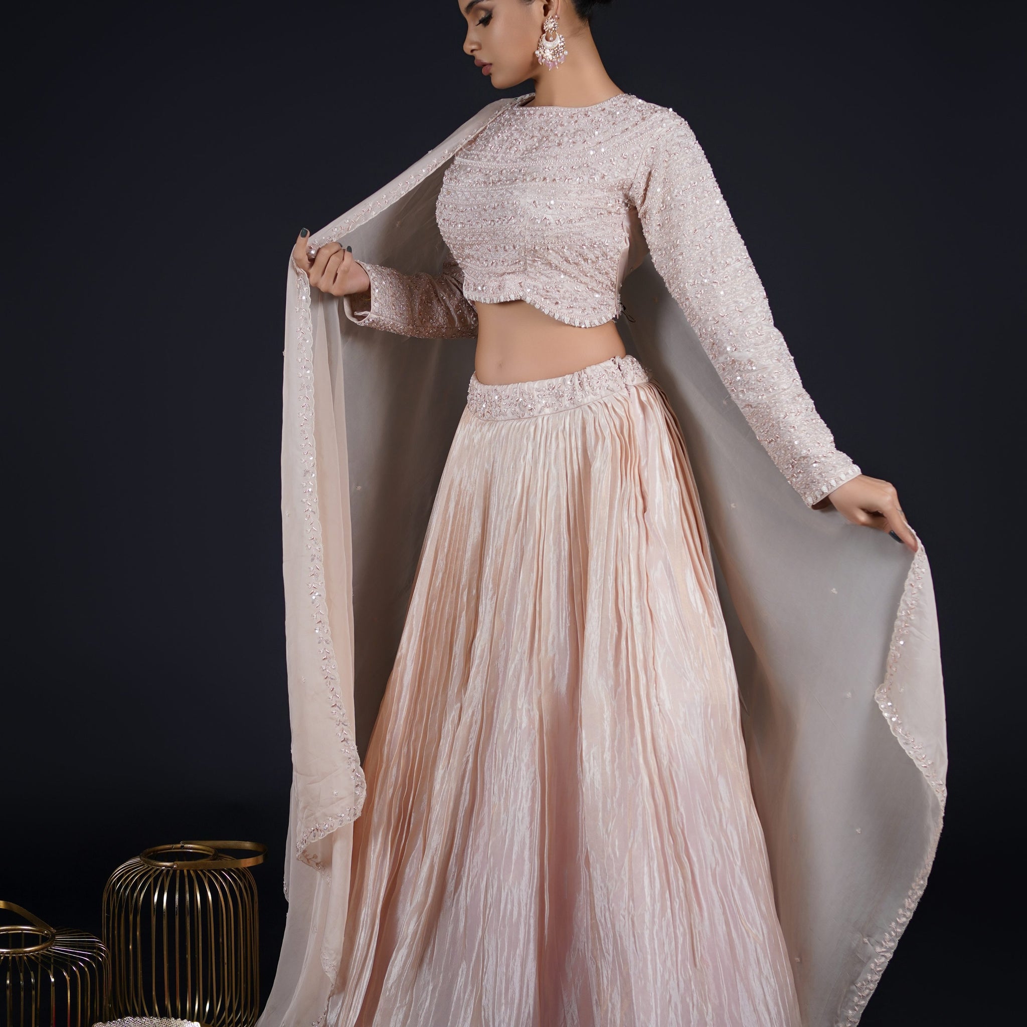 Model posing gracefully in a Tissue Rose Pink Lehenga with a full-sleeved choli and organza dupatta, adorned with pearls, sequins, and zardozi.